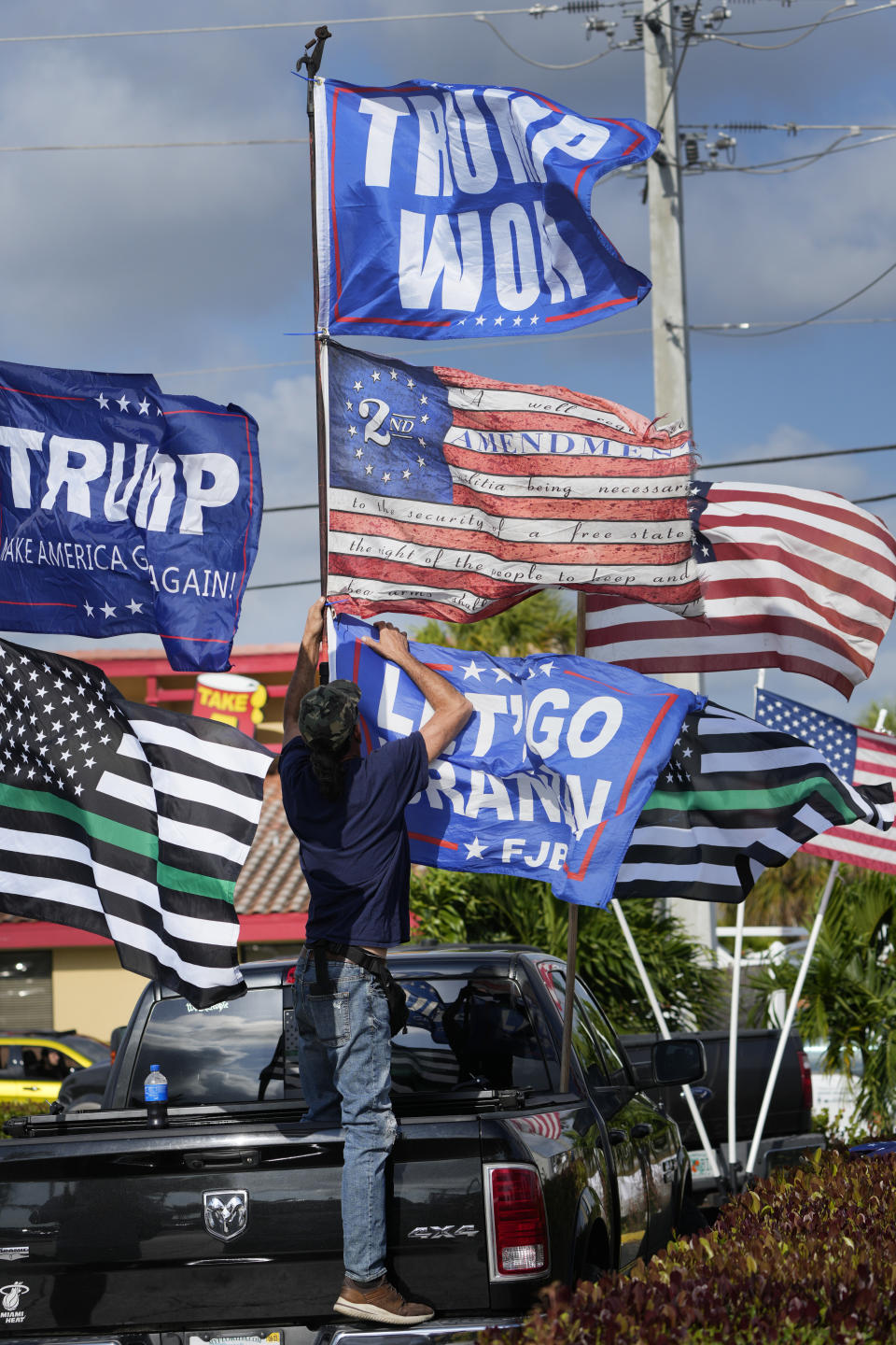 Robert Tabano, a supporter of former President Donald Trump, puts up flags at a rally, Monday, April 3, 2023, in West Palm Beach, Fla. (AP Photo/Wilfredo Lee)