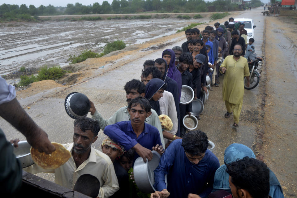 Un grupo de personas espera para recibir comida distribuida por voluntarios en el exterior de un campo para desplazados antes de la llegada del ciclón Biparjoy, en Sujawal, en la provincia de Sindh, Pakistán, el 15 de junio de 2023. (AP Foto/Pervez Masih)