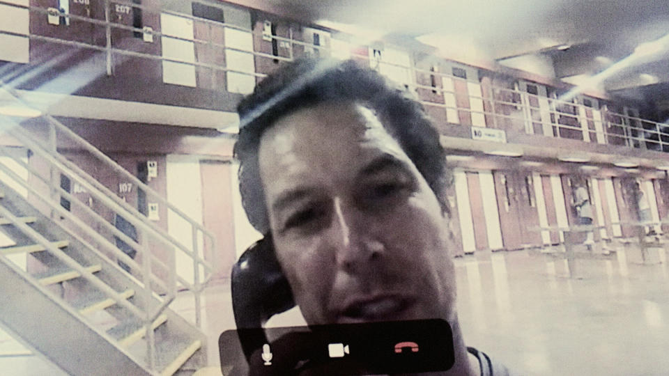 A grainy photo shows Scott Peterson holding a phone to his ear in what appears to be the inside of a prison.