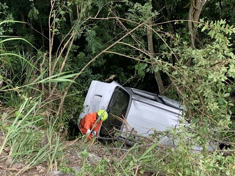 新竹司馬庫斯往秀巒方向林道26日發生一起休旅車意外翻落邊坡事故，休旅車車身受困且被大樹擋住，消防人員先用繩索固定休旅車，確保不會滑落，並持續救援。（新竹縣消防局提供）