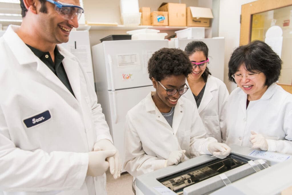 This photo provided by UMBC, University of Maryland, Baltimore County (UMBC) Professor Weihong Lin, second from left, works with students in her biological sciences lab. (Marlayna Demond/UMBC via AP)