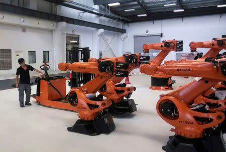 FILE PHOTO: A staff member stands next to robots at a plant of Kuka Robotics in Shanghai, China August 13, 2014. REUTERS/Pete Sweeney/File Photo