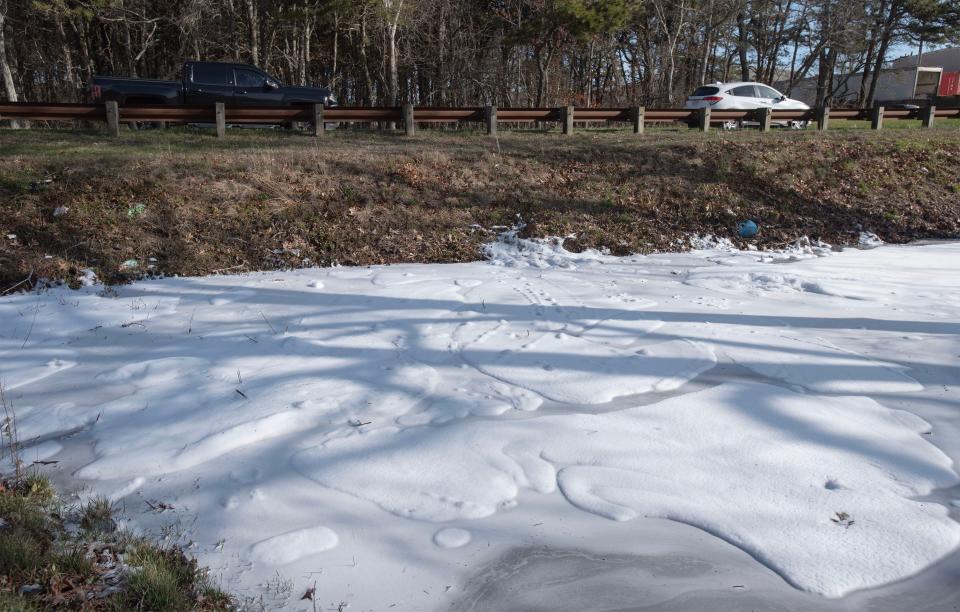 Firefighting foam tops a roadway catch pool off the side of Great Western Road in South Dennis Wednesday morning across the street from the scene of a storage bay fire on Tuesday. Residents in the area were given a water advisory because of runoff from the fire.