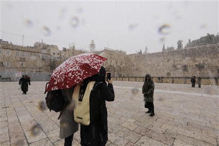 A woman has her picture taken as snow falls near the Western Wall in Jerusalem's Old City December 12, 2013. REUTERS/Ammar Awad