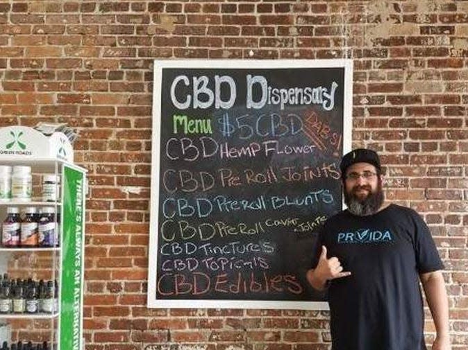 Carlos Hermida stands in front of a CBD menu in his Hemp and mushroom dispensary, Chillum