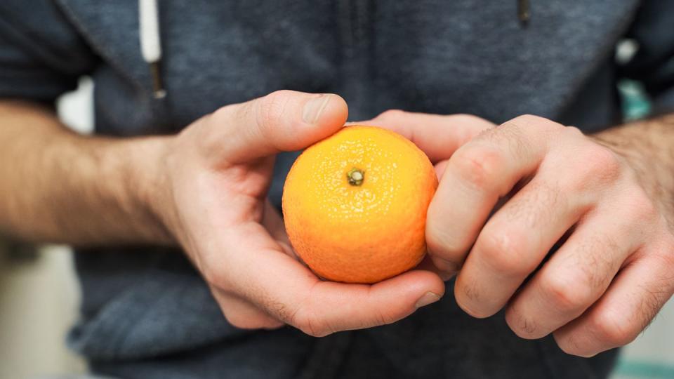 close up view of a man holding a bright, juicy orange in his hands