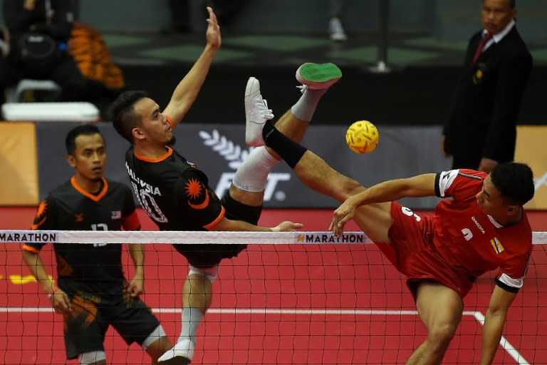 Malaysia's Mohd Hanafiah (C) hits the ball past Mohd Aliffuddin Jamaludin (R) of Brunei during their men's Sepaktakraw team Regu round-robin match of the 29th Southeast Asian Games (SEA Games) at the Titiwangsa stadium in Kuala Lumpur on August 18