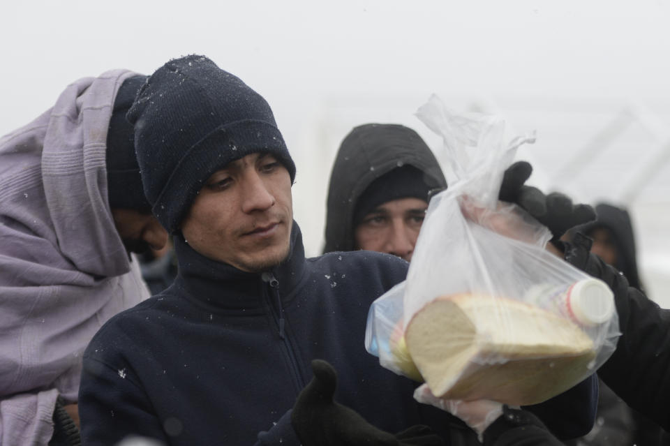 Migrants receive food handouts during snowfall at the Lipa camp, outside Bihac, Bosnia, Friday, Jan. 8, 2021. A fresh spate of snowy and very cold winter weather on has brought more misery for hundreds of migrants who have been stuck for days in a burnt out camp in northwest Bosnia waiting for heating and other facilities. (AP Photo/Kemal Softic)