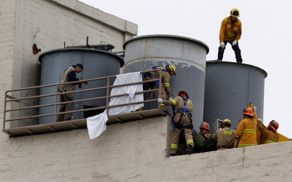Firefighters work to remove a body found inside a water tank on the rooftop of Hotel Cecil - Alamy