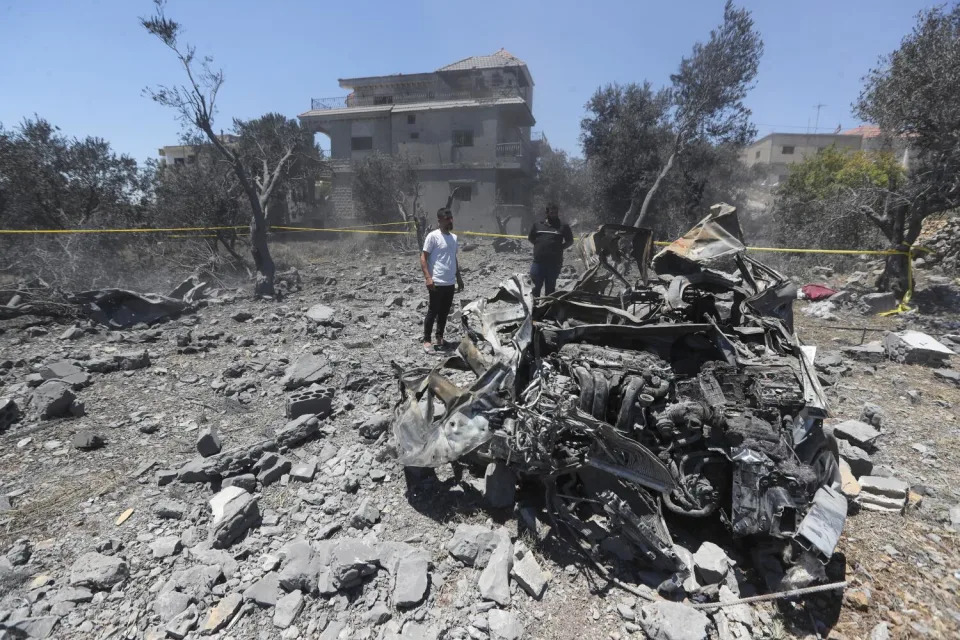 People stand next to a destroyed car that was hit by an Israeli airstrike in Jmaijmeh, Lebanon.