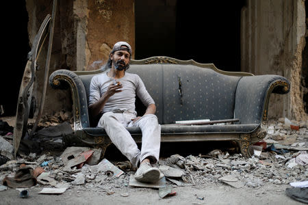 Abu Nimr, 36, smokes a cigarette as he sits on a sofa along a damaged street in Yarmouk Palestinian camp in Damascus, Syria October 10, 2018. Picture taken October 10, 2018. REUTERS/Omar Sanadiki