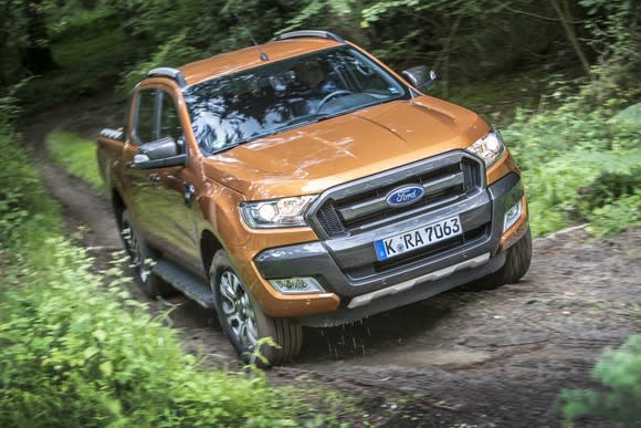 An orange Ford Ranger pickup with European license plates driving on a muddy trail.