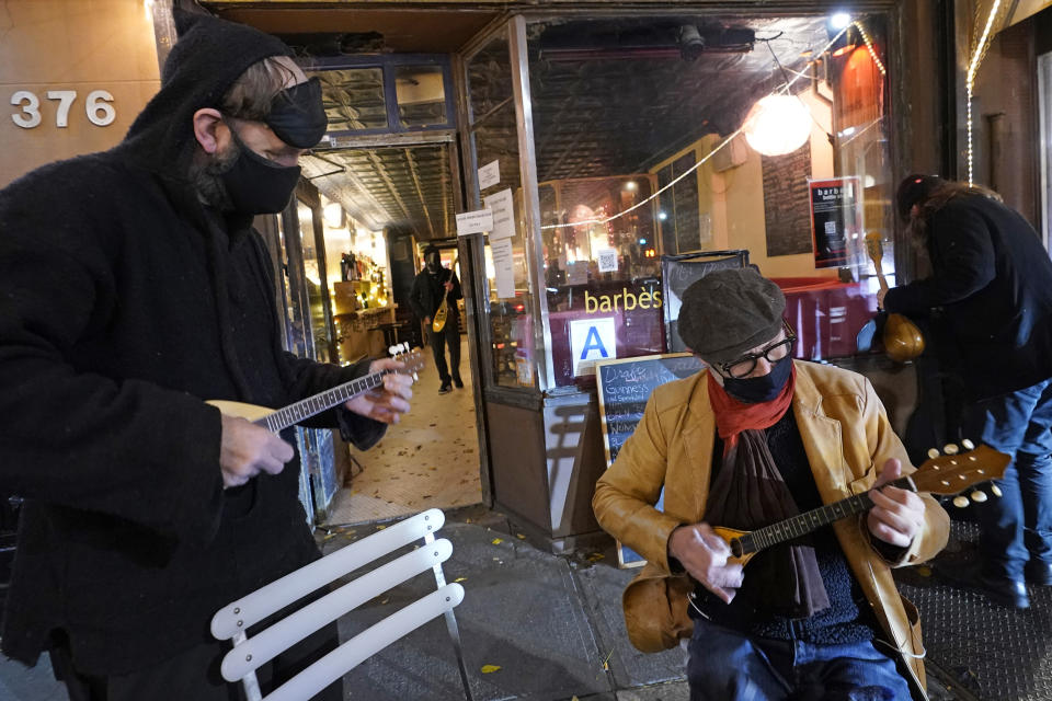A band member, left, joins Olivier Conan, center, as the pair strum baglamas, stringed instruments from Greece and Turkey similar to lutes, outside the entrance to Barbès, a popular neighborhood music venue and bar that Conan recently converted to a bottle shop, Tuesday, Dec. 1, 2020, in the Brooklyn borough of New York. (AP Photo/Kathy Willens)