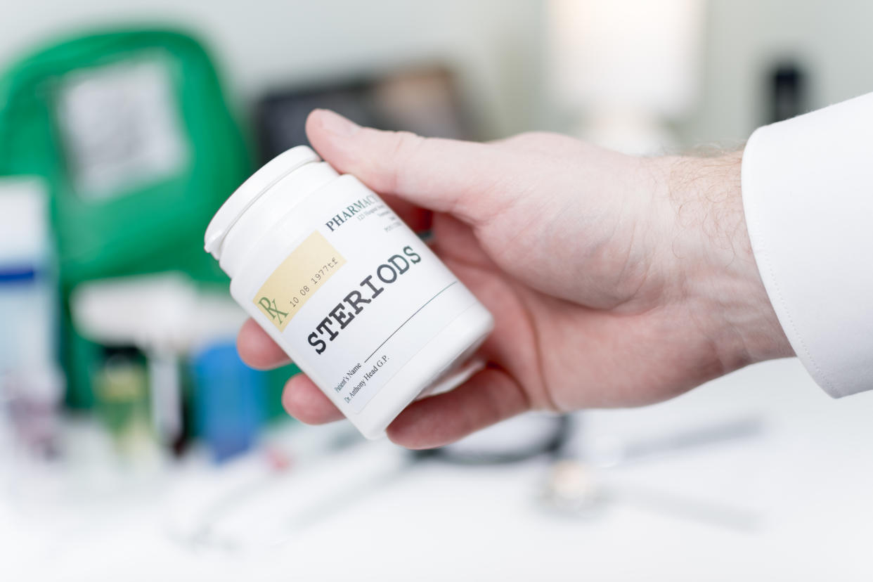 Showing a hand holding steroids medicine in a doctor's office/medical setting.