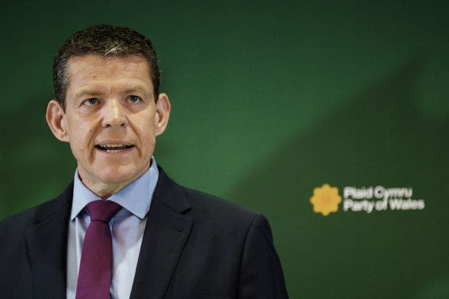 Rhun ap Iorwerth standing in front of a green Plaid Cymru backdrop