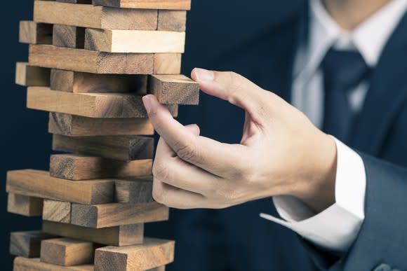 A businessman pulls out a Jenga piece.