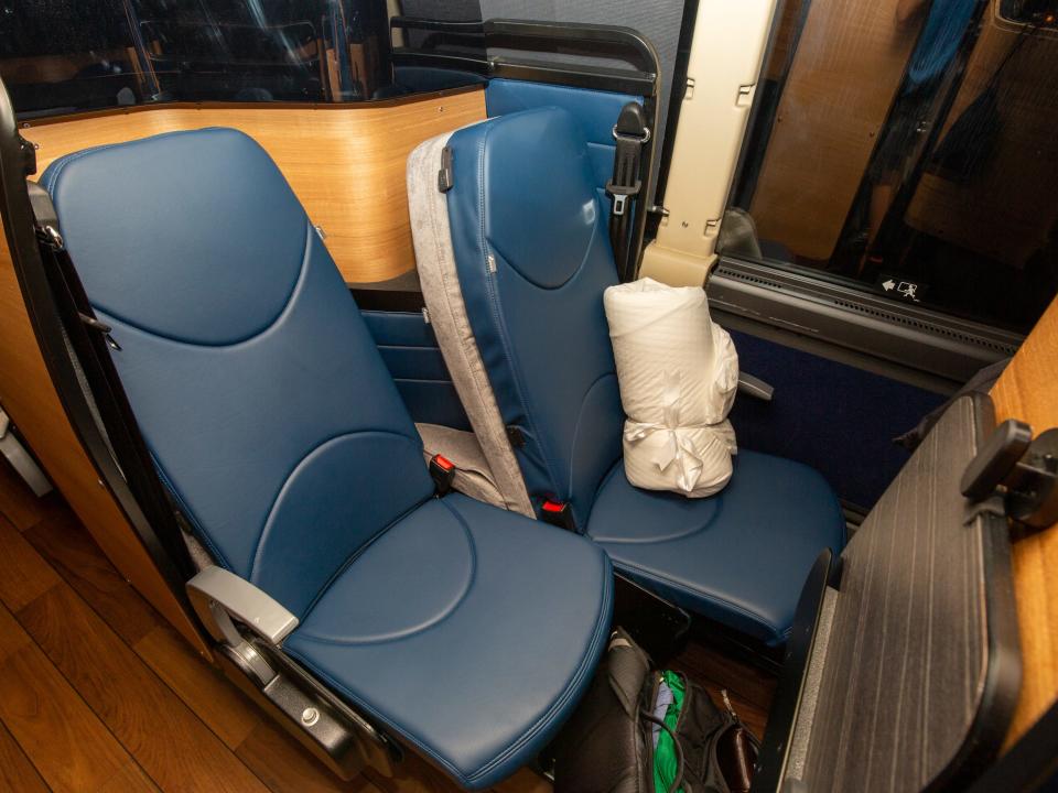 Two staggered bus seats with a bundle of sheets on one of the seats.