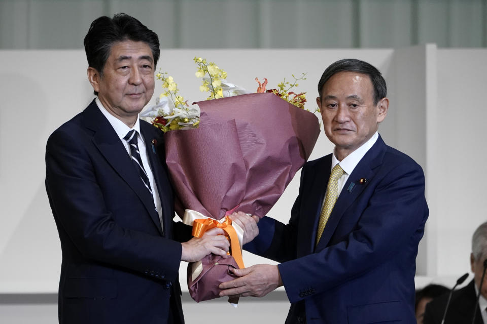 Japan's Prime Minister Shinzo Abe, left, receives flowers from Chief Cabinet Secretary Yoshihide Suga after Suga was elected as new head of Japan's ruling party at the Liberal Democratic Party's (LDP) leadership election Monday, Sept. 14, 2020, in Tokyo. The ruling LDP chooses its new leader in an internal vote to pick a successor to Prime Minister Shinzo Abe, who announced his intention to resign last month due to illness. (AP Photo/Eugene Hoshiko, Pool)