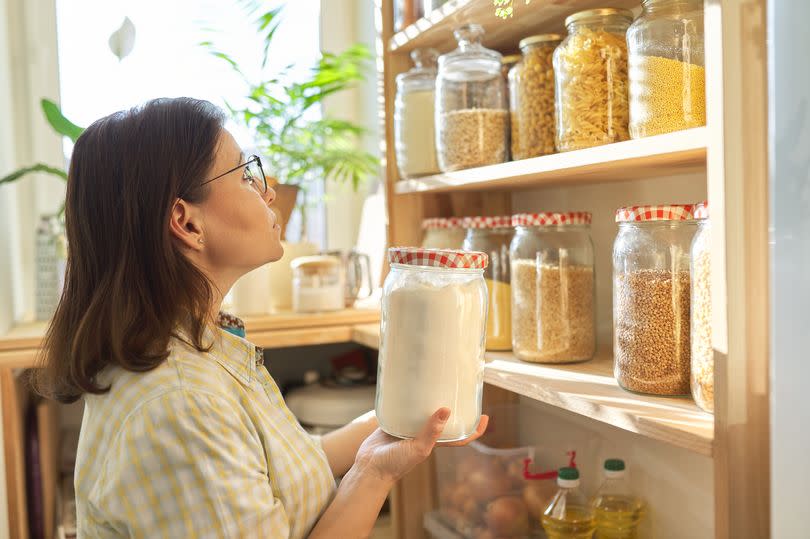 Food storage, wooden shelf in pantry with grain products in storage jars. Woman taking food for cooking