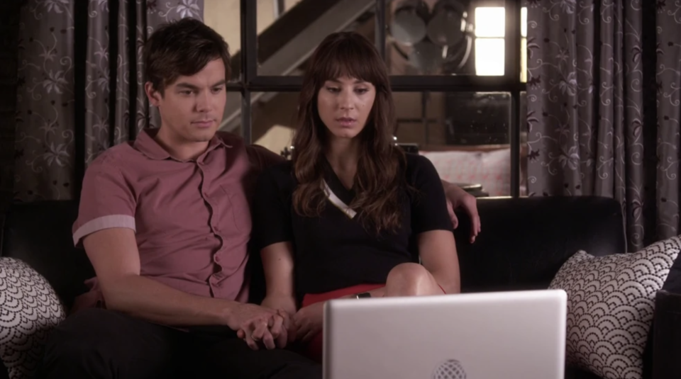Caleb and Spencer sitting on a couch, holding hands, and looking at a laptop
