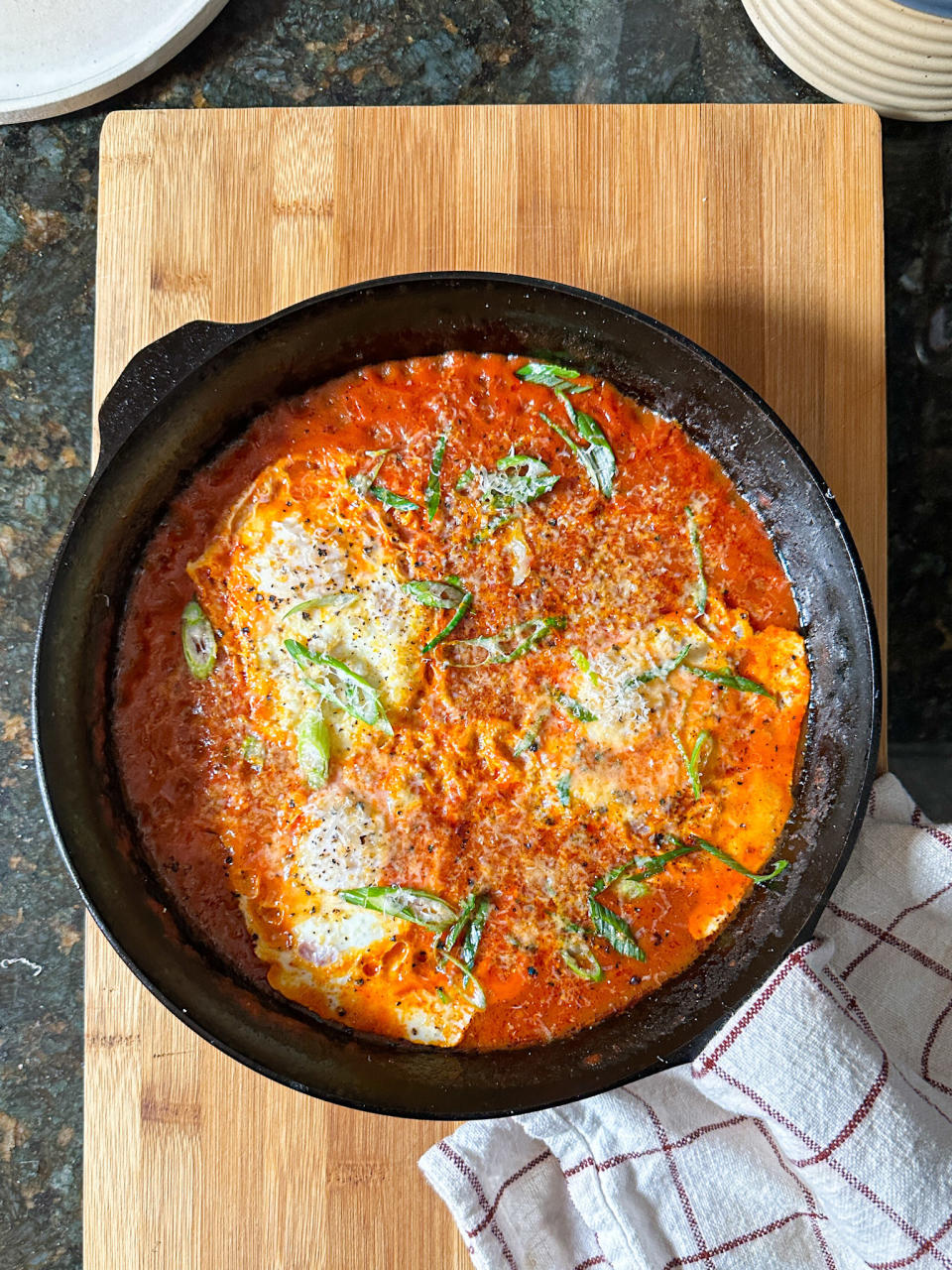 runny poached eggs in a tomato sauce in cast iron skillet, topped with scallions and parmesan cheese