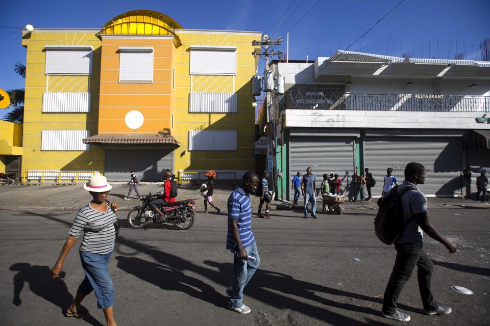 Residents walk past closed businesses on the third day of a strike and of countrywide protests over allegations of government corruption, in Port-au-Prince, Haiti, Tuesday, Nov. 20, 2018. Demonstrators are calling for the president to resign for not investigating allegations of corruption in the previous government over a Venezuelan subsidized energy program, Petrocaribe. (AP Photo/Dieu Nalio Chery)