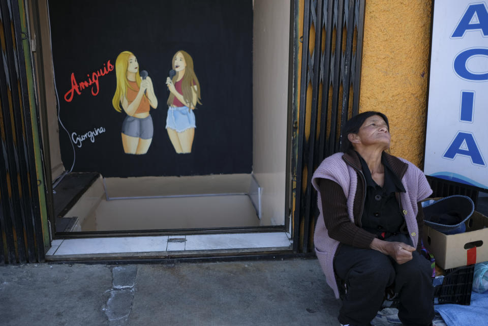 A woman sits at the entrance of a restaurant in La Paz, Bolivia, Friday, June 28, 2024, two days after Army troops stormed the government palace in what President Luis Arce called a coup attempt.(AP Photo/Carlos Sanchez)