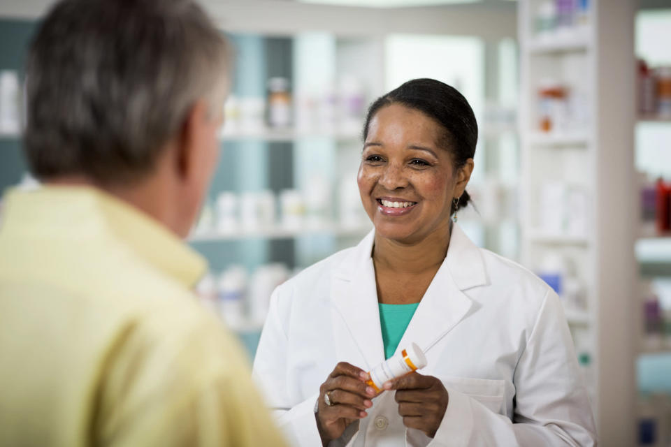 A pharmacist holding a prescription bottle while speaking with a customer.