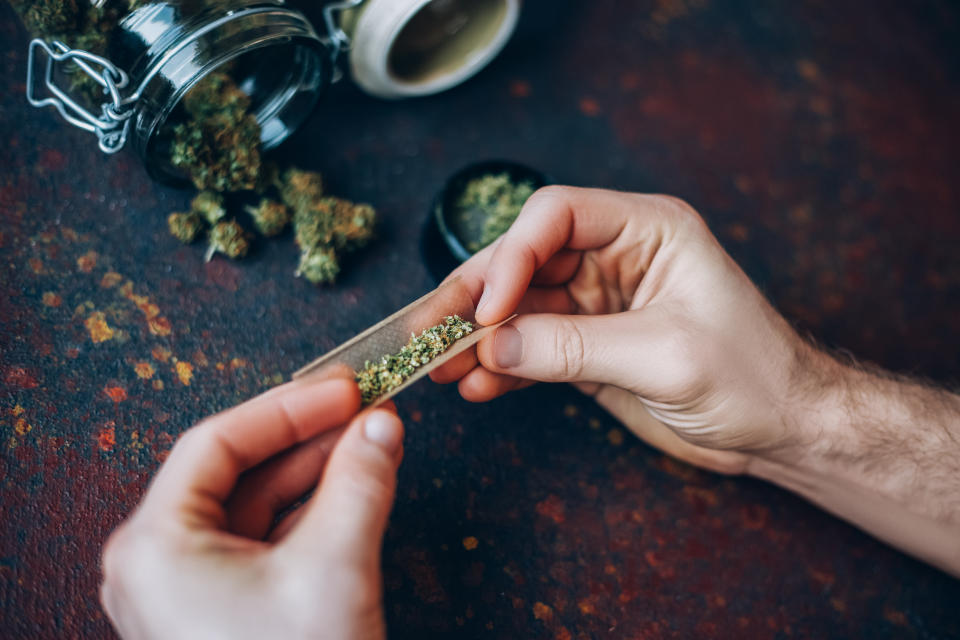 Man's hands twist marijuana into a cigar on dark background