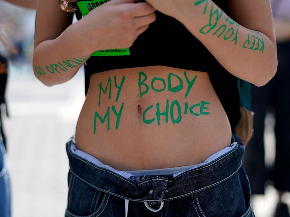 A person's bare stomach bears the words "my body my choice" in green paint.