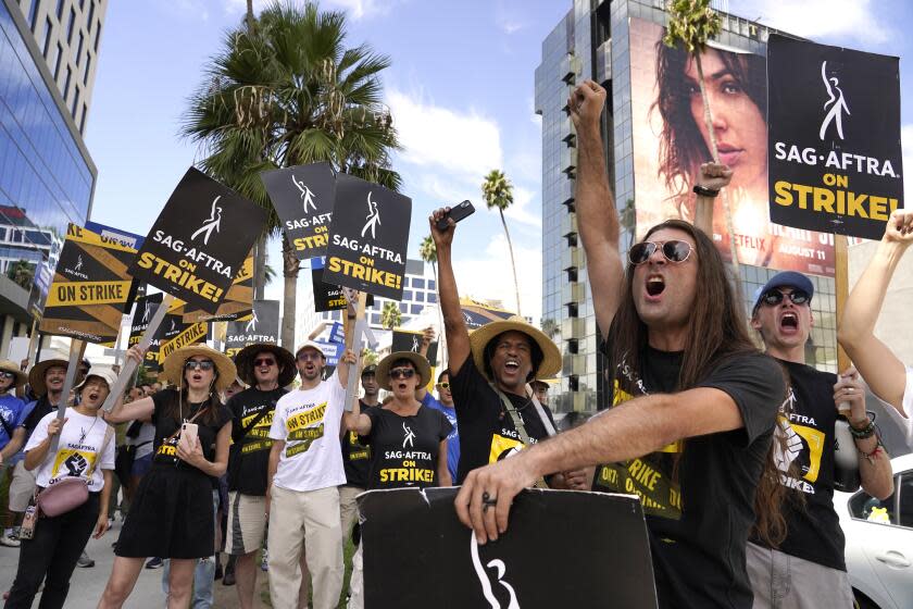 A group of picketers raise their fists in the air while carrying signs that read, "SAG-AFTRA on Strike!"