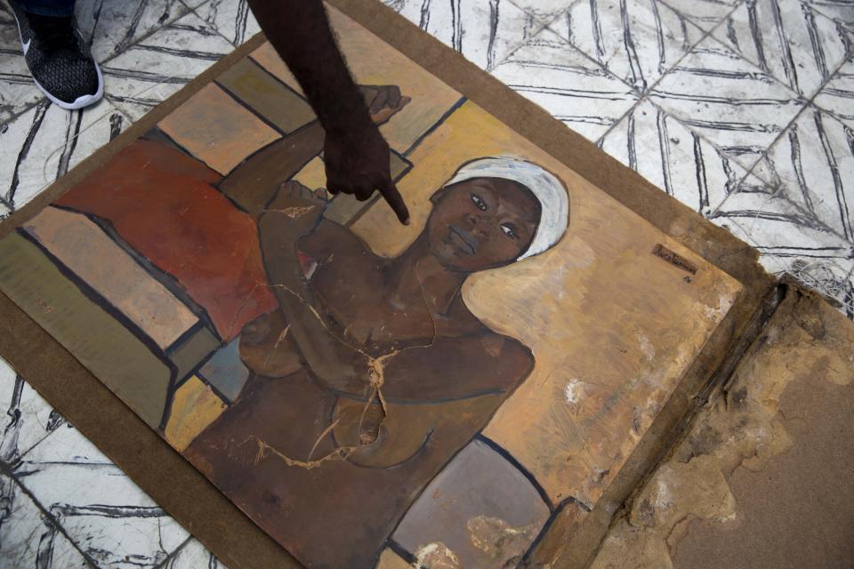 In this July 4, 2019 photo, Berthony Vilbrun points at a painting that was damaged during the earthquake 2010, at the Musée d'Art du Collège Saint Pierre, in Port-au-Prince, Haiti. The museum has only recently opened a tiny room to display a handful of paintings. (AP Photo/Dieu Nalio Chery)