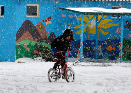 A stranded refugee boy rides his bicycle through a snowstorm at a refugee camp north of Athens January 10, 2017.REUTERS/Yannis Behrakis