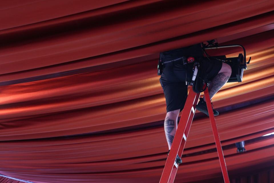 Man up on a ladder works on a light among fabric hanging from the ceiling