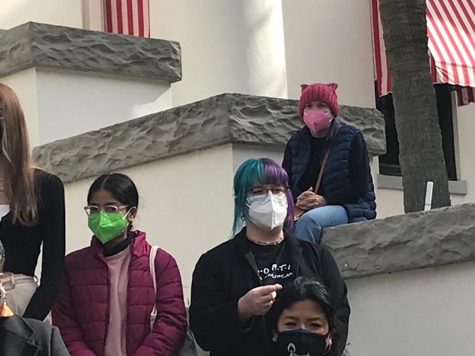 Marty Monroe, pink mask, sits on the Capitol steps during a rally to oppose a proposed 15-week abortion ban