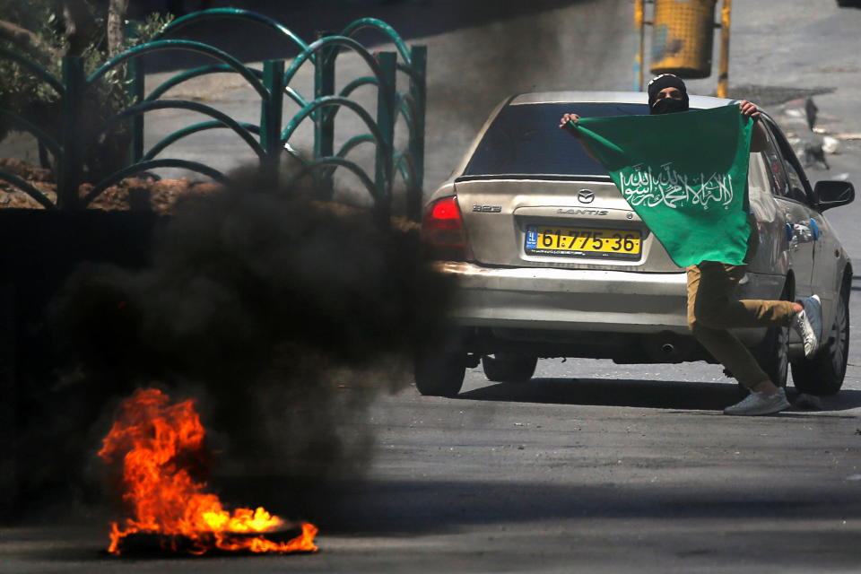 A Palestinian demonstrator holds a Hamas flag as he runs during a protest over cross-border violence between Palestinian militants in Gaza and the Israeli military, in Hebron, in the Israeli-occupied West Bank on May 18, 2021. / Credit: MUSSA ISSA QAWASMA/REUTERS