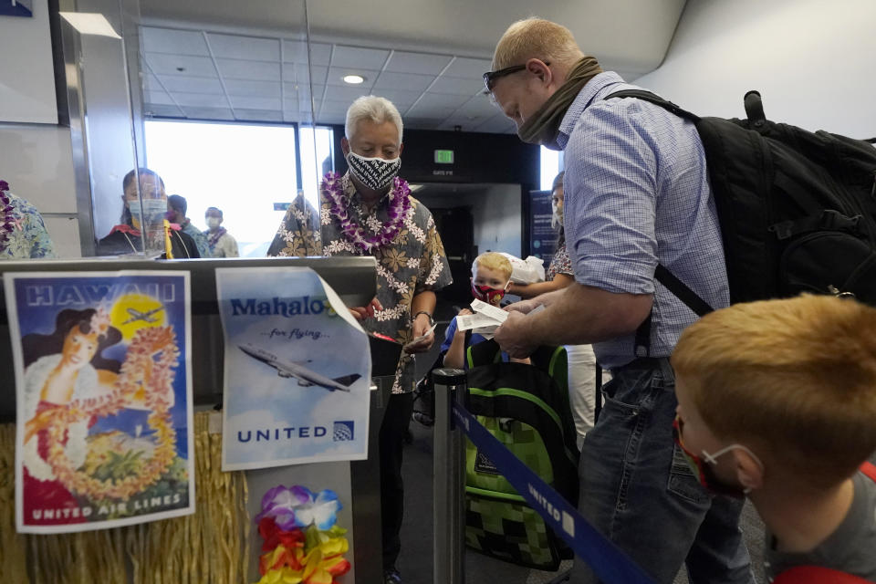 A United Airlines agent checks in passengers at the gate to board a flight to Hawaii at San Francisco International Airport in San Francisco, Thursday, Oct. 15, 2020. Coronavirus weary residents and struggling business owners in Hawaii will be watching closely as tourists begin to return to the islands on Thursday without having to self-quarantine upon arrival. (AP Photo/Jeff Chiu)