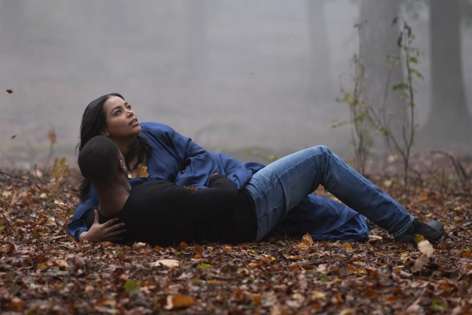 Michael B. Jordan and Lauren London lie on leaf-covered ground amid trees and fog.