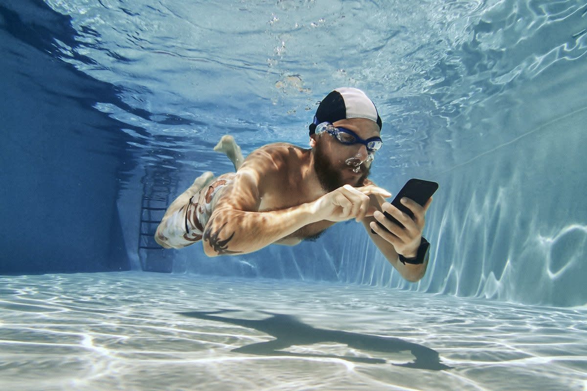 A man types on his phone underwater. 