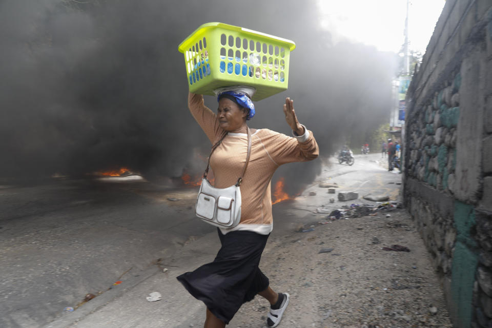 A woman walks past burning tires during a protest against Haitian Prime Minister Ariel Henry in Port-au-Prince, Haiti, Monday, Feb. 5, 2024. Protests have shut down major cities in Haiti as demonstrators clash with police and demand the resignation of Prime Minister Ariel Henry. (AP Photo/Odelyn Joseph)