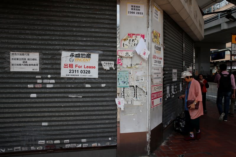 A woman stands in front of a closed shop available for lease in Hong Kong