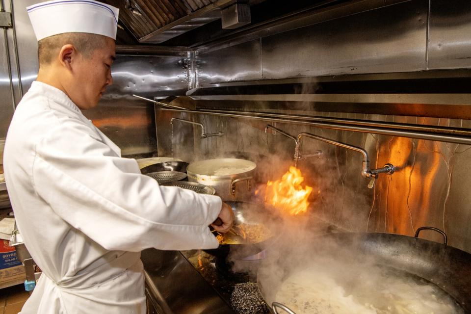 A chef cooks with a wok in the kitchen at Chengdu Taste.