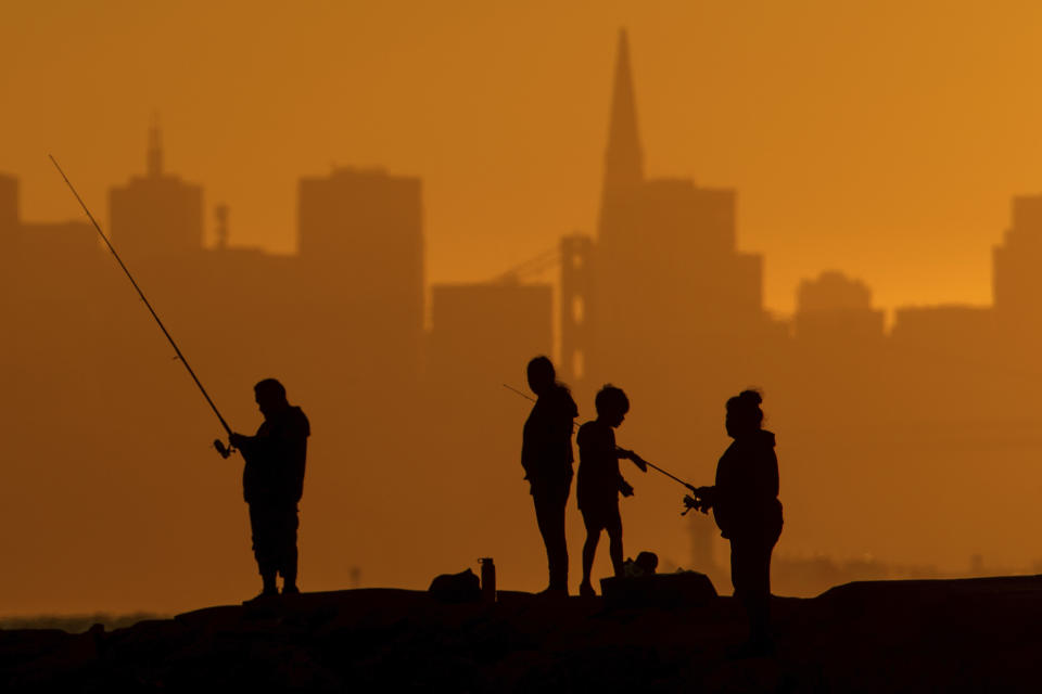 With the San Francisco skyline behind them, people fish off a jetty Monday, July 1, 2024, in Alameda, Calif. An extended heatwave predicted to blanket Northern California has resulted in red flag fire warnings and the possibility of power shutoffs beginning Tuesday. (AP Photo/Noah Berger)