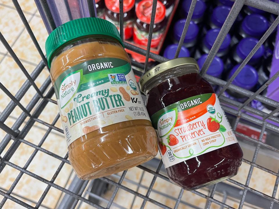 A jar of organic Simply Nature creamy peanut butter and organic Simply Nature strawberry preserves in a shopping cart.