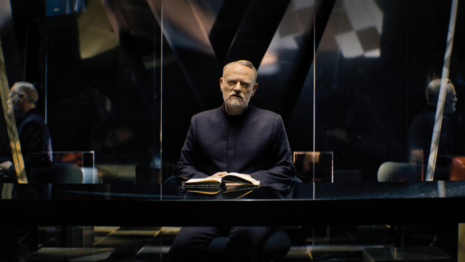 Jared Harris sits at a desk in a glossy black room in Foundation.