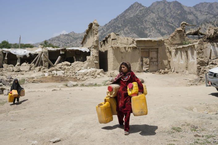 Afghan girl carries canisters in front of destroyed homes after an earthquake in Gayan district in Paktika province, Afghanistan, Sunday, June 26, 2022. A powerful earthquake struck a rugged, mountainous region of eastern Afghanistan early Wednesday, flattening stone and mud-brick homes in the country's deadliest quake in two decades, the state-run news agency reported. (AP Photo/Ebrahim Nooroozi)