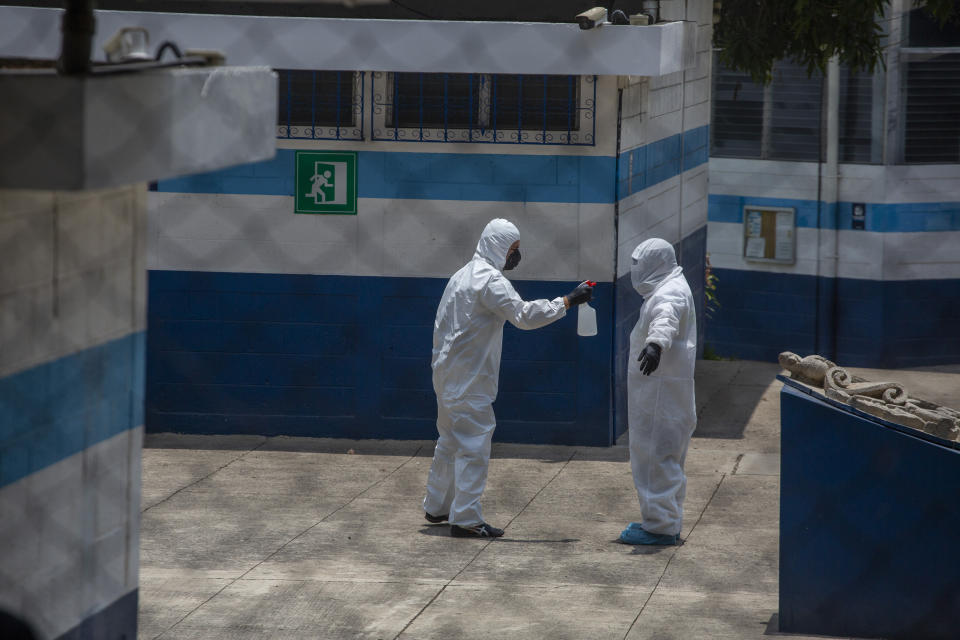 Health workers dressed in protective gear from head to toe, take turns disinfecting each other at a temporary shelter for Guatemalan citizens deported from the United States where deportees must wait for their new coronavirus test results, in Guatemala City, Thursday, April 16, 2020. Guatemala's health minister said on Tuesday that deportees from the U.S. were driving up the country's COVID-19 caseload. (AP Photo/Moises Castillo)