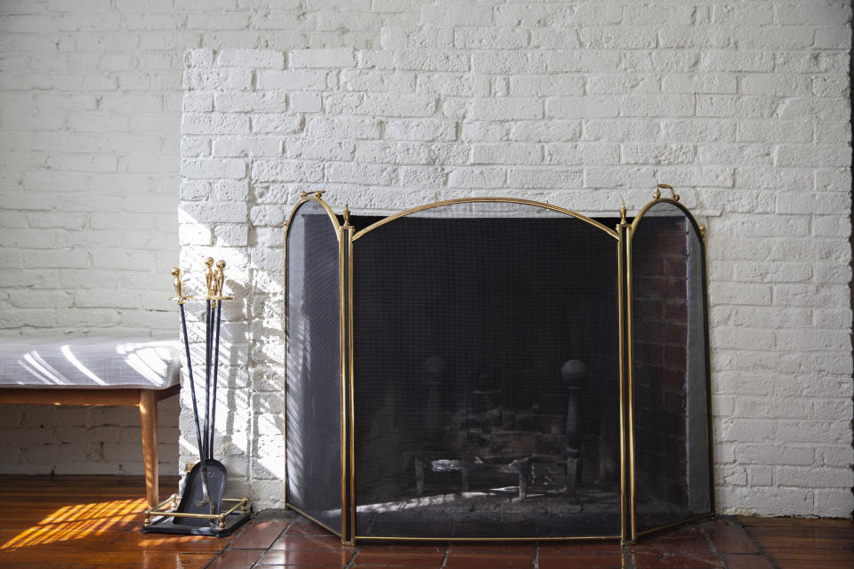 Fireplace with mesh screen and tools on white brick wall, next to wooden bench