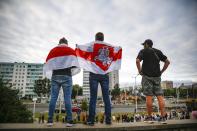 CORRECTING COUNTRY IN CAPTION TO BELARUS - People cover themselves by old Belarusian, centre, and with Belarusian National national flags, a symbol of opposition, as they gather in a street protesting the election results in Minsk, Belarus, Wednesday, Aug. 12, 2020. The demonstrators are contesting the official count showing President Alexander Lukashenko winning a sixth term with 80% of Sunday's vote, with crowds taking to the streets every night since to demand a recount. (AP Photo)