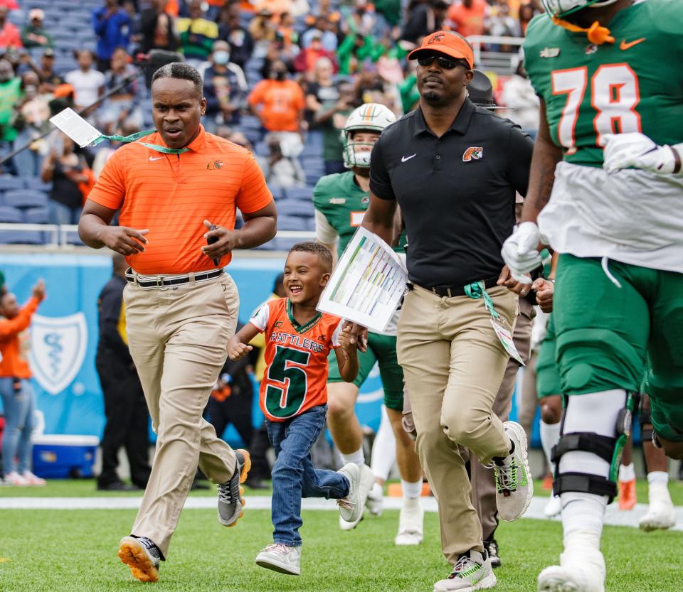 Florida A&M Rattlers head coach Willie Simmons, right,  and his son Champ run onto the field before kickoff. The Florida A&M Rattlers defeated the Bethune Cookman Wildcats 46-21 during the Florida Classic at Camping World Stadium on Saturday, Nov. 20, 2021.